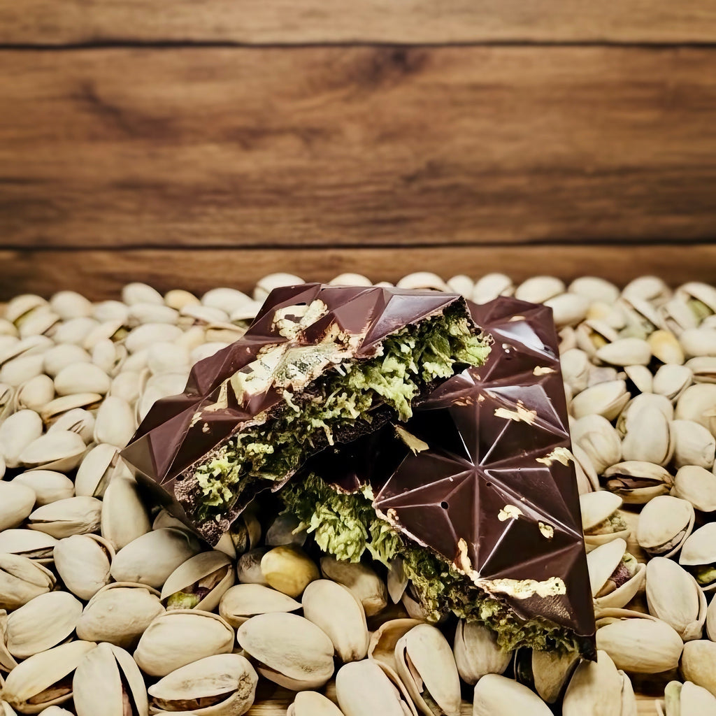 Dark chocolate bars with green toppings on a bed of pistachios against a wooden background