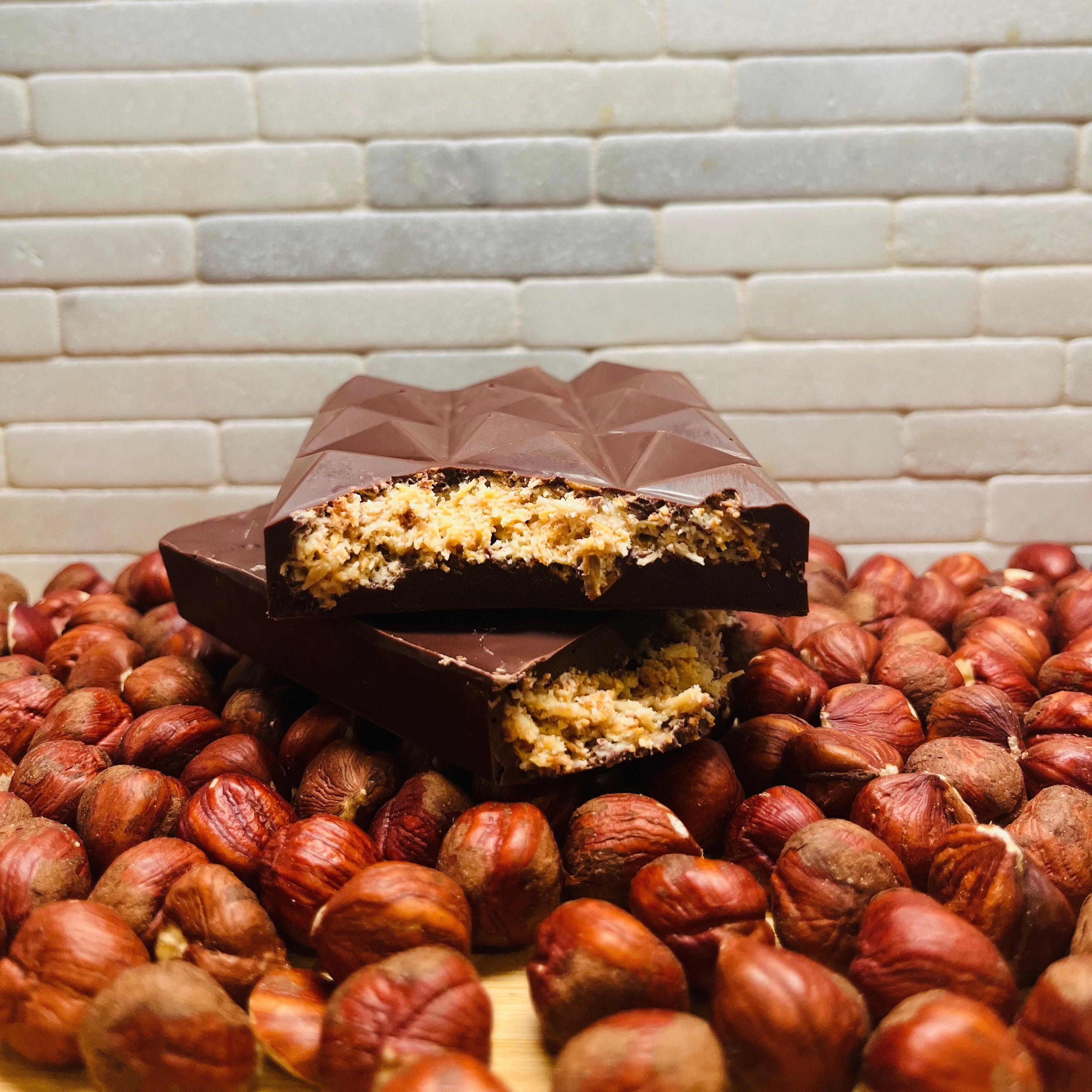 Chocolate bar with a crumbly interior on a bed of nuts against a tiled wall background